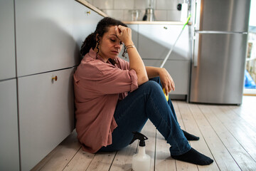 Tired young mixed woman sitting on the floor after cleaning the kitchen