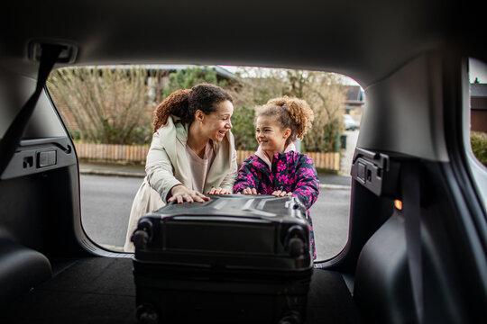 Young mother and daughter putting their suitcase in the trunk of car for a trip