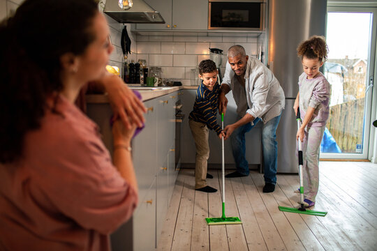 Young father teaching his kids how to sweep the floor at home