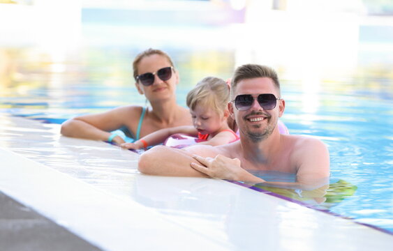 Smiling parents with their child are standing near side of pool. Family travel water park concept