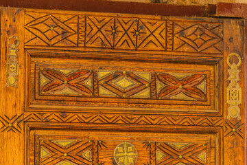 Big old wooden door decorated with various symbolic signs carved directly on the canvas of massif. Example of exterior and interior decoration of entrance lobbies in different cultures around world