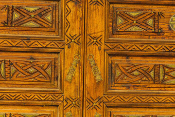 Big old wooden door decorated with various symbolic signs carved directly on the canvas of massif. Example of exterior and interior decoration of entrance lobbies in different cultures around world