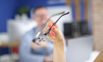 Woman's hand with bright nails holds glasses. Selection of glasses for vision concept