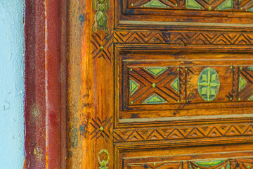 Big old wooden door decorated with various symbolic signs carved directly on the canvas of massif. Example of exterior and interior decoration of entrance lobbies in different cultures around world