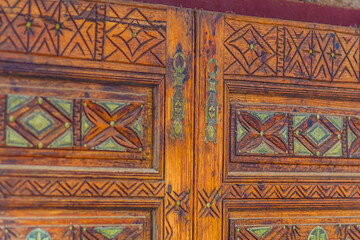 Big old wooden door decorated with various symbolic signs carved directly on the canvas of massif. Example of exterior and interior decoration of entrance lobbies in different cultures around world