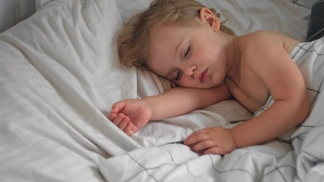 Peaceful adorable baby sleeping on a bed at home. Slumbering little child. Two years old girl sleeps peaceful at domestic room interior background. Serene dream. Cute face close up. Deep kid slumber	
