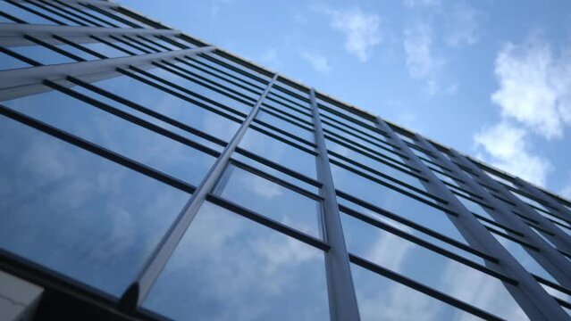 Smooth camera movement in front of the windows of an office building reflecting a sunny blue sky with white puffy clouds. 4k