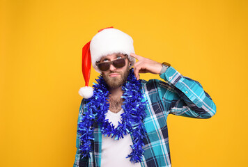 attractive young bearded man in santa hat, sunglasses, blue boa and shirt with thoughtful face on...