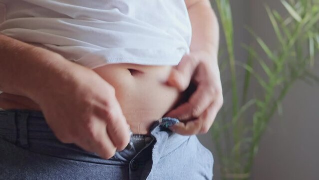 Overweight man trying to fasten too small attire in home interior chubby figure had led to tight trousers efforts to combat obesity weight problem was a top priority to improve his well-being.