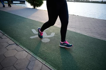 Deurstickers Close up view of woman legs on jogging paths in a park with beautiful markings on sunny day © Василь Івасюк