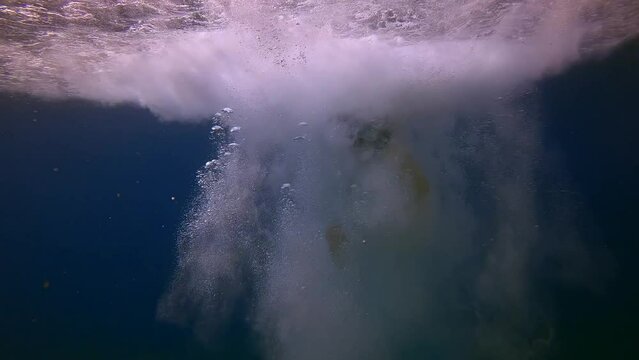 Boy dives into water and sinks to blue water in cloud of bubbles. Active male child diving underwater at blue sea with bubbles enjoying summer outdoor extreme sport, Slow motion, Mediterranean sea