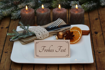 Tischdekoration zum Weihnachtsfest. Besteck mit Teller brennenden Kerzen und dem Text Frohes Fest...