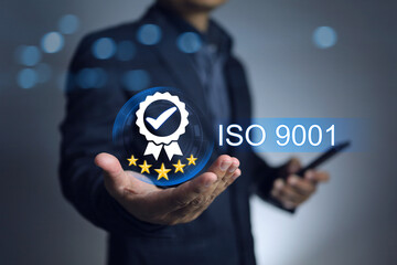 Quality control and assurance concept. Businessman holding certificate sign of iso 9001 on hand represent to good quality of products and service from factory and production line process.