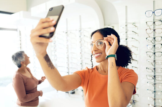 Selfie, optometry and woman trying glasses with prescription lenses and frame in an optical store. Vision, smile and young female person taking a picture on a phone for choosing spectacles in clinic.