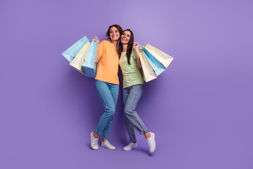 Full length cadre of of optimistic young girls spend weekend italian fashion week shopping hobby isolated on purple color background