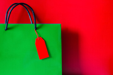Green shopping paper bag with red blank price tag on red background for Black Friday shopping sale...