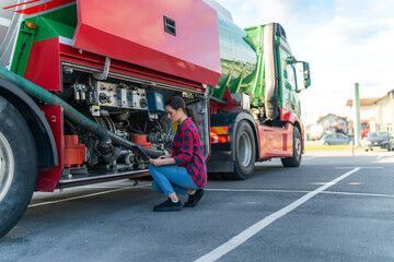 Truck driver holding a laptop,crouching next to the truck and checking the fuel level in the tank, security checks for the safe transport of cargo - obrazy, fototapety, plakaty