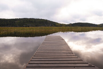 Wooden pier on a calm windless lake in the early morning. Cloudy sky.