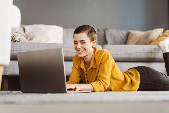 Young Modern Woman with Short Hair Laughing at Laptop on Apartment Floor