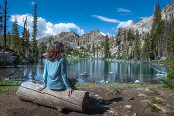 a young girl sitting on top of a wooden log overlooking a mountain lake - Powered by Adobe