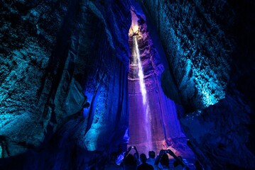 tourists in cave under blue lights and waterfall photo by jeff evans