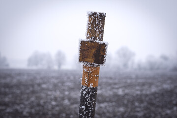 Close up image of black and yellow pole marking a gas line in middle of frosty field