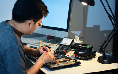computer technician Motherboard repairman wearing glasses is using an IC meter to find defects on...