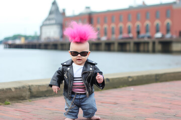Amusing punk baby with leather jacket in street, displaying rebellious hairstyle. - obrazy, fototapety, plakaty