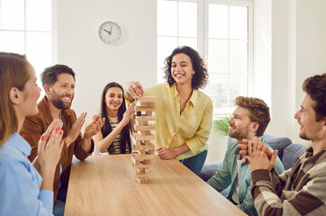 Happy joyful young students friends guys and girls playing together with wooden building blocks at home sitting at the table enjoying time together. Home leisure and board games concept.