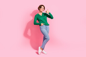 Full length photo of young lady wearing green shirt with jeans showing thumb up like feedback her outfit isolated on pink color background