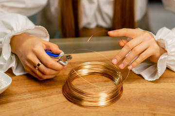 close-up hands of a young girl  makes jewelry with her own hands cuts the remnants of wire for a...