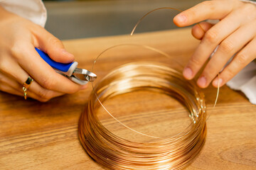 close-up hands of a young girl  makes jewelry with her own hands cuts the remnants of wire for a...