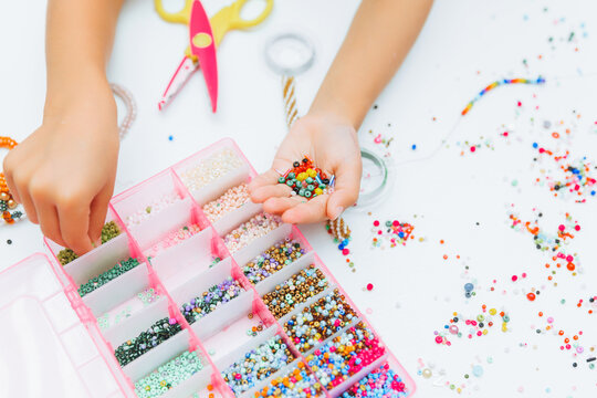 Cute little blonde girl making bead jewelry at a table in the room