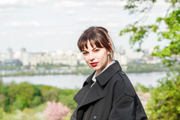 A beautiful girl drinks coffee at the table, in a raincoat, in a white shirt, in black trousers with suspenders