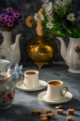 Fototapeta na wymiar Two cups of Turkish coffee on a gray ground and a group of white utensils and flowers