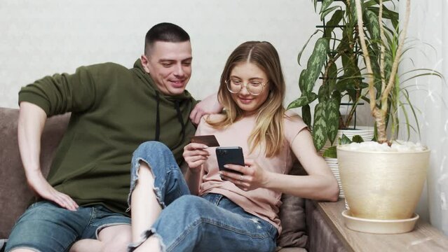 Happy online retail web services buyers make easy purchase, instant money transfer, use secure remote e payment concept. Couple in love sit on sofa with laptop holding credit card buying on internet