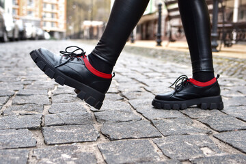 woman's legs in black shoes walking along a city road.