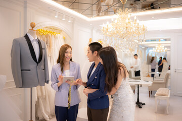 In a wedding dress shop, an Asian LGBT couple looks at the groom's suit to wear on his wedding day.