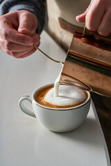 Close-up photo of a person preparing a cup of latte and coffee