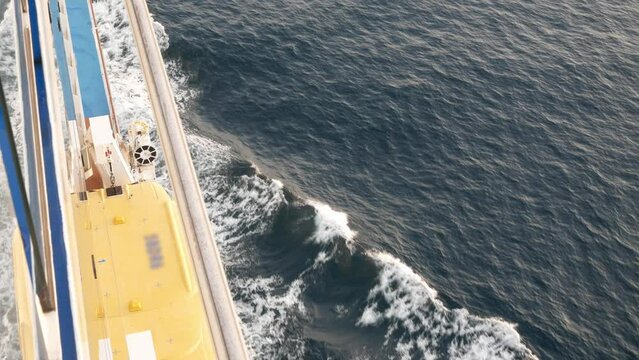 Lifeboat on giant cruise ship view down to ocean surface with waves below while ship cruising saling in the sea. safety muster lifeboat equipment.