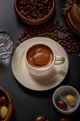 Close-up photo of a white Turkish coffee cup on a black background with copper pots and roasted coffee beans