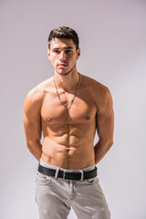 A shirtless handsome young man posing for a picture showing muscular torso, looking at camera,...