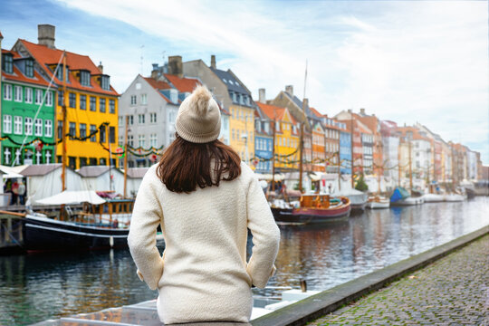 A tourist woman with coat enjoys the view to the colorful Nyhavn area in Copenhagen, Denmark, during christmas winter time