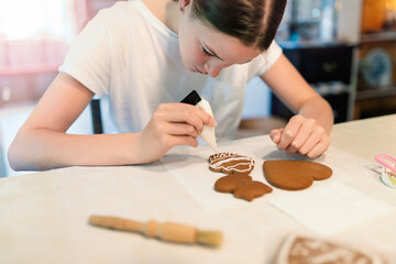 Girl decorating gingerbread cookies with icing sugar. Selective focus. - 661068499