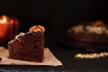 Piece of chocolate cake with walnuts on a dark background. Selective focus. Bokeh background. Sweet homemade cakes for the holiday. Snack for tea or coffee.