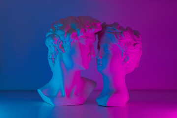 Two antique statue's heads in pink and blue colored neon light. Relationships of man and woman. Love, romance, kiss, tenderness. Modern design. Contemporary art. David and Aphrodite