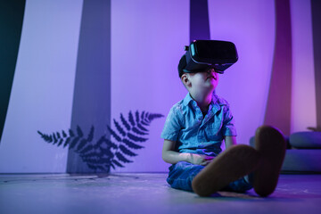 Little boy wearing VR headset sitting on the floor in the museum playroom, engaged exploring...