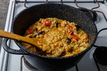 Braised eggplants with meat and rice with dogwood Israeli style in a cast-iron high frying pan with a wooden spatula.