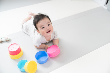 自然光が入るリビングのプレイマットで知育おもちゃを使って遊ぶご機嫌笑顔な生後8か月の赤ちゃん	