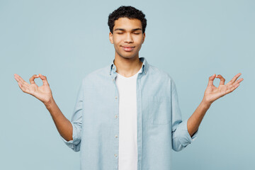 Young spiritual man of African American ethnicity in shirt white t-shirt casual clothes hold spread hands in yoga om aum gesture relax meditate try calm down isolated on plain pastel blue background
